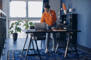 Kendine güvenen genç kadın cep telefonuyla konuşurken ve ofiste teknoloji kullanırken meşgul.