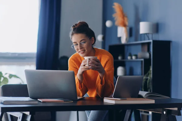 美しい女性がコーヒーカップを保持し オフィスで彼女の職場に座っている間 ラップトップを使用して — ストック写真