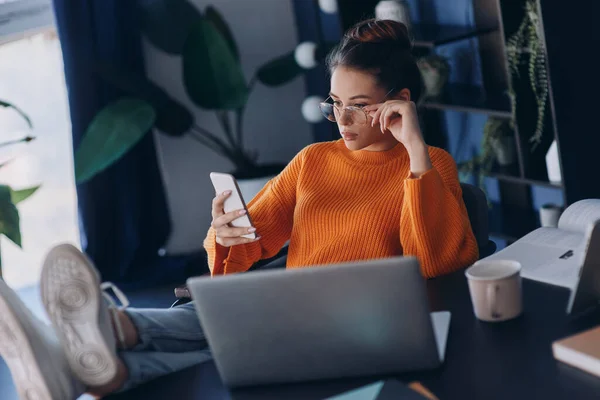 Självsäker Ung Kvinna Håller Fötterna Skrivbordet Medan Använder Smarttelefon Kontoret — Stockfoto