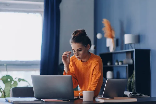 Skoncentrowana Młoda Kobieta Dopasowująca Okulary Patrząca Laptopa Podczas Pracy Biurze — Zdjęcie stockowe