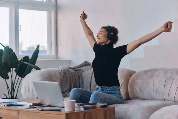 Счастливая Молодая Женщина Наушниках Держит Руки Поднятыми Сидя Рядом Ноутбуком — стоковое фото