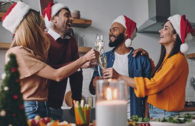 Neşeli gençler evde Noel yemeğinin tadını çıkarırken şampanyayla kadeh kaldırıyorlar.