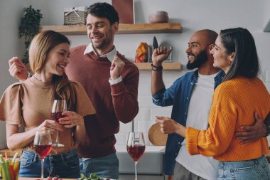 Neşeli gençler evde eğlenirken dans ediyor ve gülümsüyor.