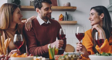 Güzel genç insanlar evde birlikte akşam yemeğinin tadını çıkarırken konuşup gülümsüyorlar.