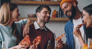 Birlikte eğlenirken pizza yiyip gülümseyen bir grup genç.