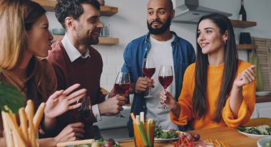 Güzel genç insanlar evde birlikte yemek yerken şarap içip sohbet ediyorlar.