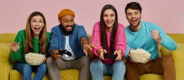 Pembe arka planda kanepede otururken video oyunu oynayan bir grup mutlu genç.