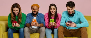 Gençlerin akıllı telefonlar kullandıkları ve kanepede otururken gülümsedikleri bir stüdyo fotoğrafı.