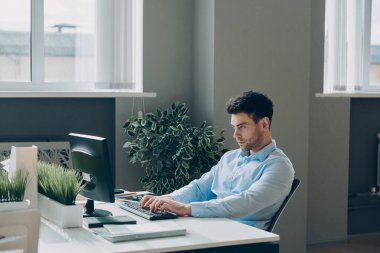 Ofisinde otururken bilgisayar kullanan konsantre genç işadamı.