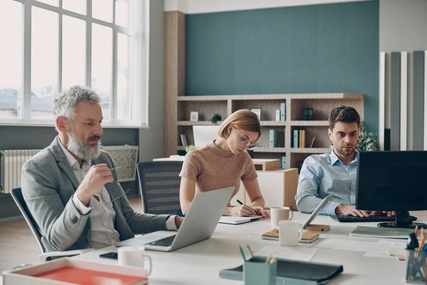 オフィスの共有デスクに座っている間に一緒に働く自信のあるビジネスの人々のグループ — ストック写真