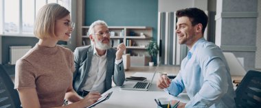 Ofis masasında otururken İK yöneticileriyle röportaj yapan neşeli genç adam.