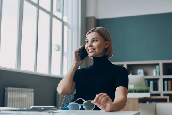 Ofiste Çalışırken Cep Telefonuyla Konuşan Gülümseyen Kendine Güvenen Bir Kadını — Stok fotoğraf