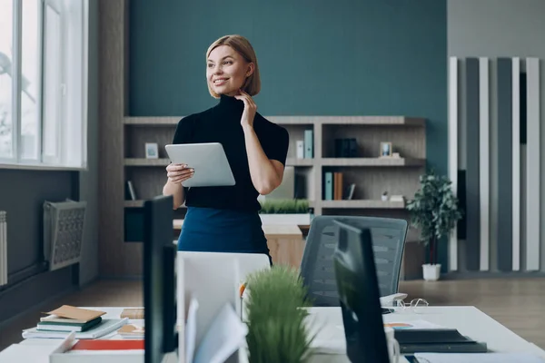 オフィスの彼女の職場の近くに立っている間幸せなビジネスマンの女性は デジタルタブレットを保持 — ストック写真