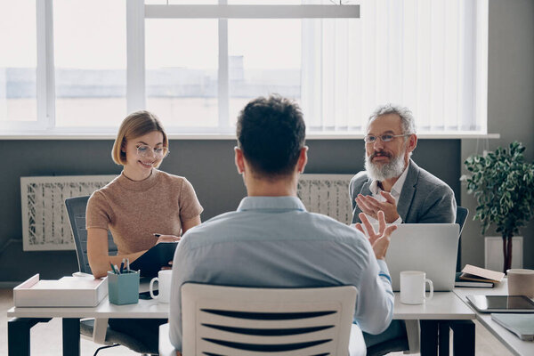 Rear view of man having interview with HR managers while sitting at the office desk