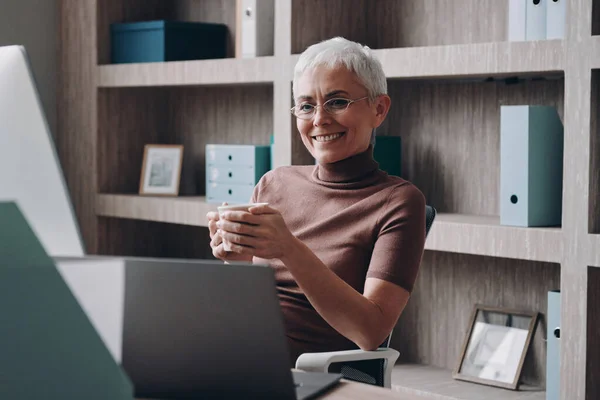 Happy Senior Businesswoman Enjoying Hot Drink While Looking Computer Monitor — Stock Photo, Image