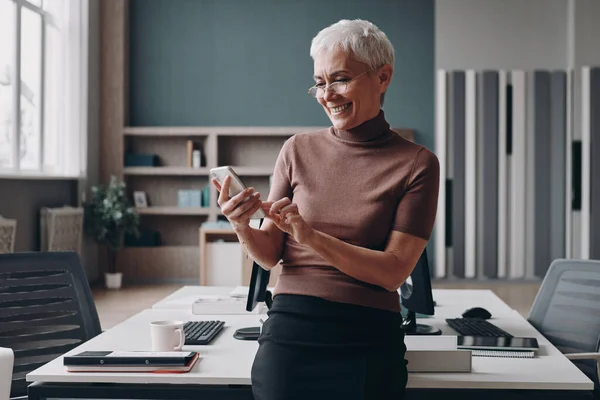 Senior Businesswoman Using Smart Phone Smiling While Leaning Office Desk — Stock Photo, Image