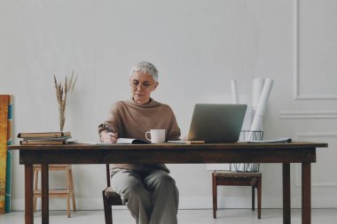 Kendine güvenen kıdemli iş kadını iş yerinde otururken notlar alıyor.