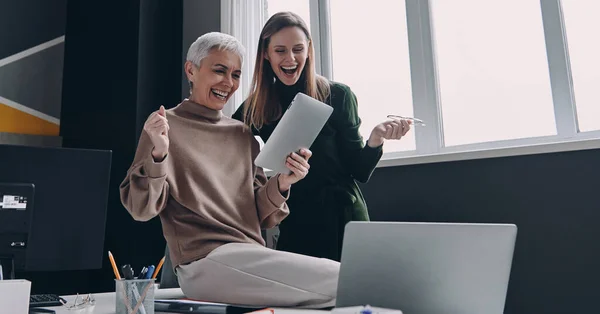オフィスで一緒に仕事をしながらデジタルタブレットとジェスチャーを見ている2人の興奮した女性 — ストック写真