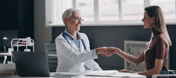 一緒に医務室に座っている間に患者と握手をする幸せな女性医師 — ストック写真