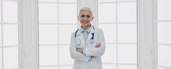 Médica Confiante Mantendo Braços Cruzados Sorrindo Contra Uma Janela — Fotografia de Stock