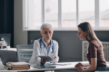 Hasta muayenehanesinde otururken reçeteyi tartışan kendinden emin bir kadın doktor.