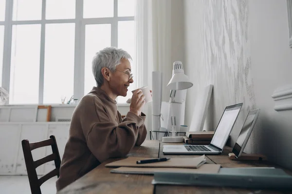 Starsza Bizneswoman Przy Kawie Uśmiechu Podczas Korzystania Laptopa Jej Miejscu — Zdjęcie stockowe