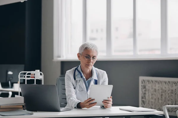 医務室の机に座っている間 デジタルタブレットを使用して女性医師を自信を持って — ストック写真