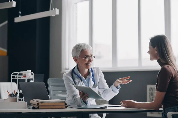 Szczęśliwa Kobieta Lekarz Rozmawia Pacjentem Siedząc Razem Gabinecie Medycznym — Zdjęcie stockowe