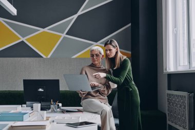 İki iş kadını birlikte çalışırken bilgisayar kullanıyor ve iletişim kuruyor.