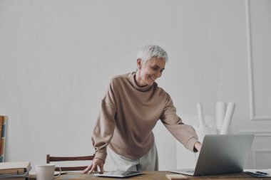 Kendine güveni tam bir iş kadını. Dizüstü bilgisayar kullanıyor ve çalıştığı yerin yanında dururken gülümsüyor.