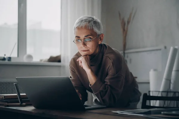 Skoncentrowana Starsza Kobieta Korzystająca Laptopa Podczas Pracy Późna Biurze — Zdjęcie stockowe