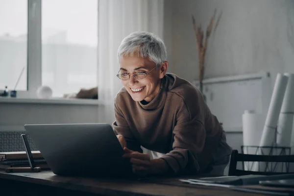 Confident Senior Woman Using Laptop Smiling While Working Late Home — Stock Photo, Image