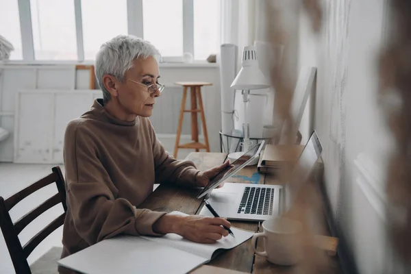 Senior Woman Making Notes Pad Looking Digital Tablet While Sitting — Stock Photo, Image