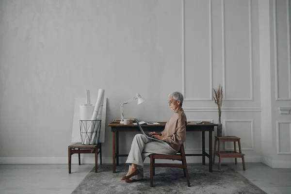 stock image Concentrated senior businesswoman using laptop while sitting at her creative working place