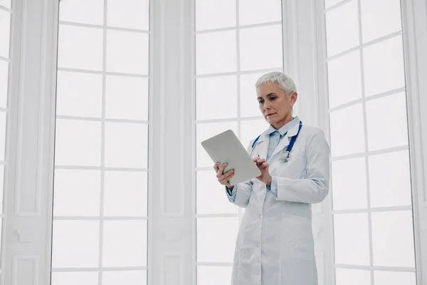 Pewna Siebie Lekarka Korzystająca Tabletu Cyfrowego Stojąca Przy Oknie — Zdjęcie stockowe