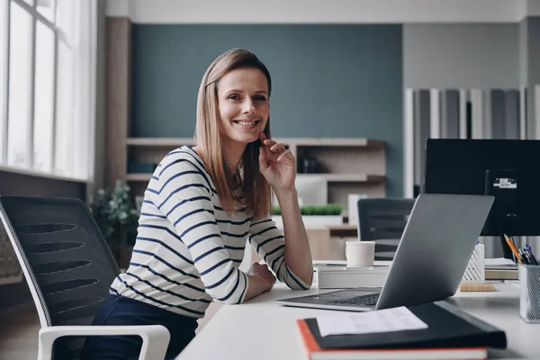 Pewna Siebie Młoda Bizneswoman Patrzy Obiektyw Uśmiecha Się Siedząc Biurze — Zdjęcie stockowe