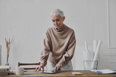 İş yerinin yanında dikilirken dijital tablet kullanan kendinden emin bir iş kadını.