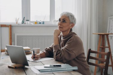 İşyerinde otururken notlar alan düşünceli kıdemli iş kadını.