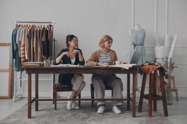 İki kadın moda tasarımcısı birlikte atölyede yeni bir koleksiyon üzerinde çalışıyorlar.