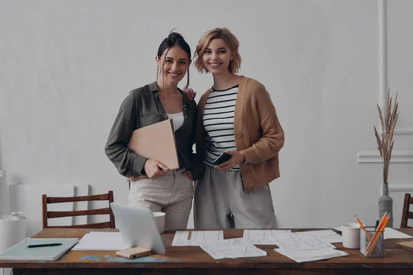 創造的な職場の近くに立っている間 2人の自信に満ちた女性の同僚は笑顔 — ストック写真