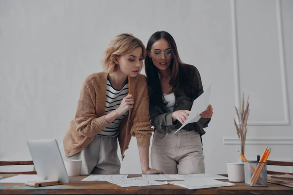 Dos Mujeres Jóvenes Confiadas Revisando Papeles Mientras Trabajan Juntas Oficina — Foto de Stock