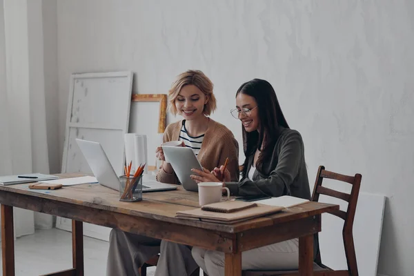 2人の幸せな若い女性が創造的なオフィスで一緒に働いている間技術を使用して — ストック写真