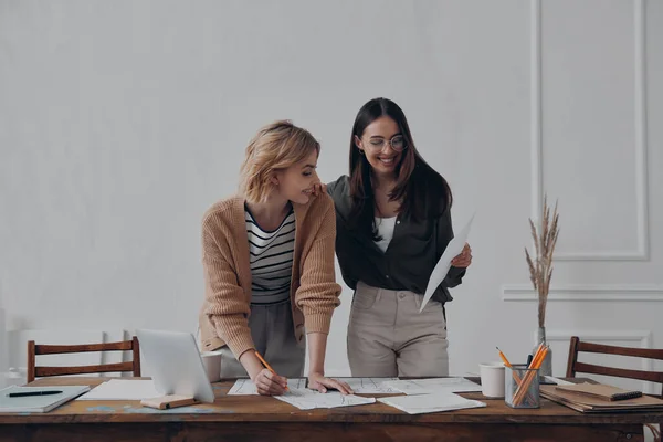 2人の幸せな若い女性が事務所の机の近くに一緒に立っている間に書類作成を行う — ストック写真