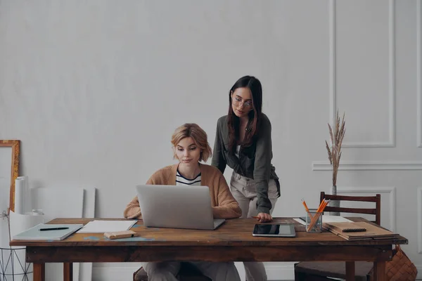 創造的なオフィスで一緒に働いている間 ラップトップを見ている2人の自信に満ちた若い女性 — ストック写真