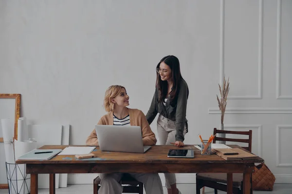 二人の美しい若い女性が一緒に創造的なオフィスで作業しながら幸せそうに見える — ストック写真