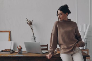 Yaratıcı ofisteki masada dizüstü bilgisayar kullanan güzel bir genç kadın.