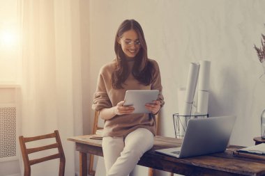 Yaratıcı ofisteki masada otururken dijital tablet üzerinde çalışan mutlu genç kadın.