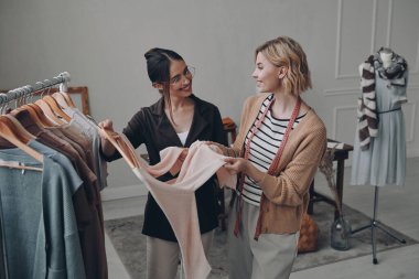 İki mutlu moda tasarımcısı atölyede çalışırken kıyafetlerini inceliyor.
