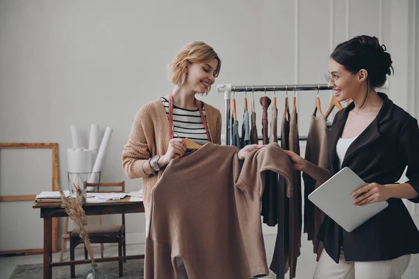 Two female fashion designers discussing clothes while working in workshop together