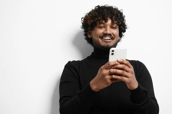 英俊潇洒的印度人站在白色背景下 一边用智能手机一边笑 — 图库照片